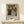 May include: Framed vintage exhibition poster featuring Renoir's family portrait painting with adults and children in period dress, displayed on light wood console table beside small white wrapped gift with evergreen sprig against cream wall