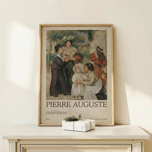 May include: Framed vintage exhibition poster featuring Renoir's family portrait painting with adults and children in period dress, displayed on light wood console table beside small white wrapped gift with evergreen sprig against cream wall