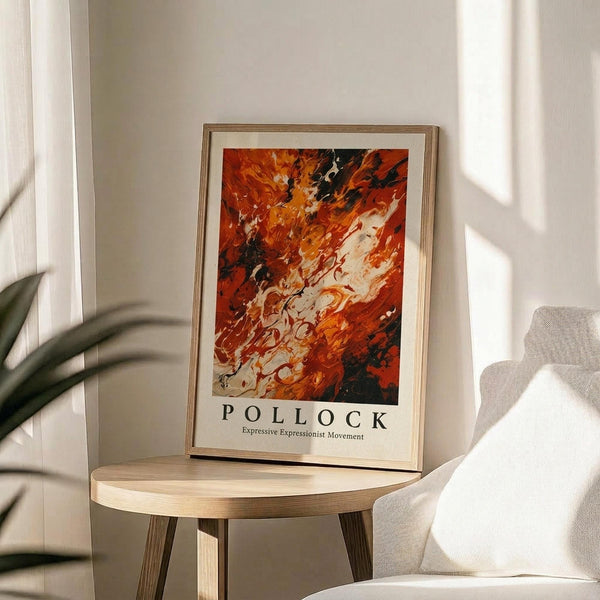 May include: Abstract expressionist art poster with vibrant orange, red, black and white paint swirls displayed in thin wooden frame on round wooden side table. Neutral beige armchair and green plant leaves visible in softly lit modern living room with white walls and natural window light creating gentle shadows.