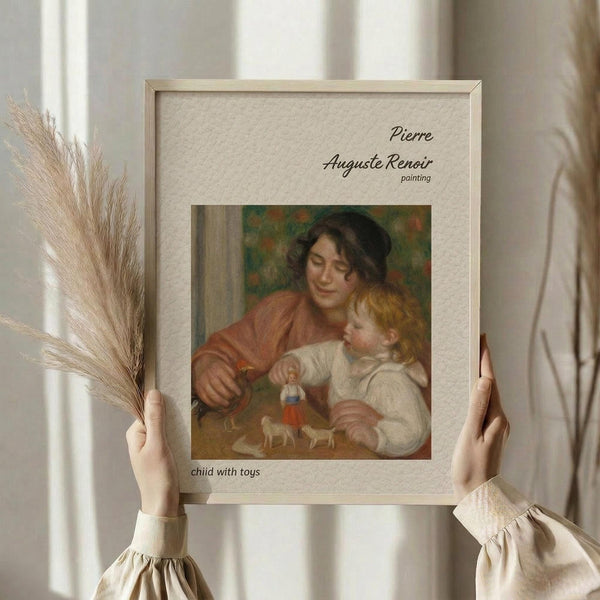 May include: Person in cream clothing holding framed Renoir reproduction and dried pampas grass against white curtained window. Classical painting shows woman in rust-colored dress with blonde child playing with small toys and figurines. Beige textured mat with elegant black script text identifying the artwork. Natural lighting creates soft, warm ambiance in minimalist interior setting.