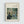 May include: Framed art print hanging on white wall showing Renoir's Impressionist painting of people dining at an outdoor restaurant. The artwork depicts figures in soft blues and greens seated at a table under latticed greenery. Light wood frame with cream matting displays the classic French scene with loose, painterly brushstrokes characteristic of the Impressionist style.