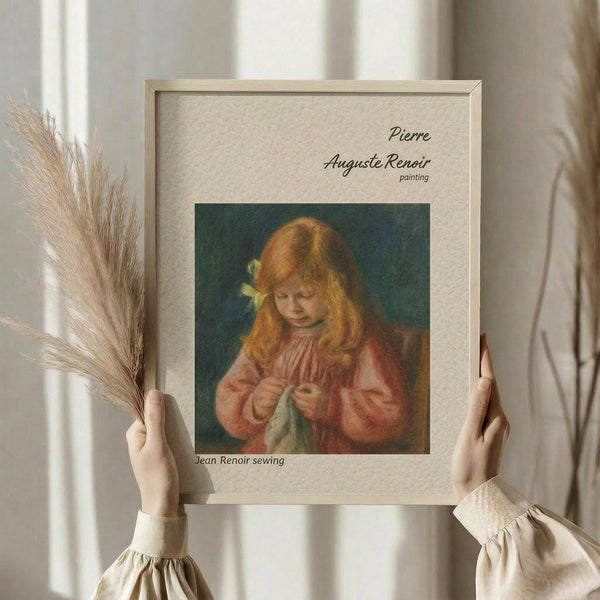 May include: Hands holding a framed art print featuring a young girl with reddish hair and yellow bow sewing green fabric, wearing a pink dress against dark background. Light wood frame with beige matting. Person in cream ruffled sleeves also holds dried wheat stalks. Soft natural lighting by white curtained window.