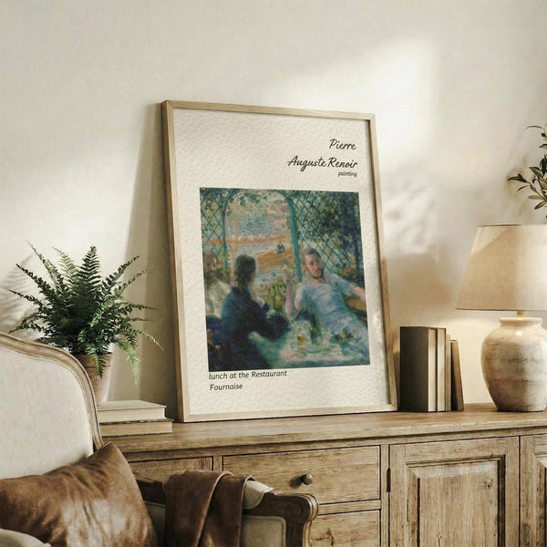 May include: Framed reproduction of Renoir's impressionist painting showing two figures dining at a restaurant terrace, displayed on a rustic wooden sideboard alongside potted ferns, stacked books, and ceramic vases in a warmly lit living room with neutral walls and brown leather furniture.
