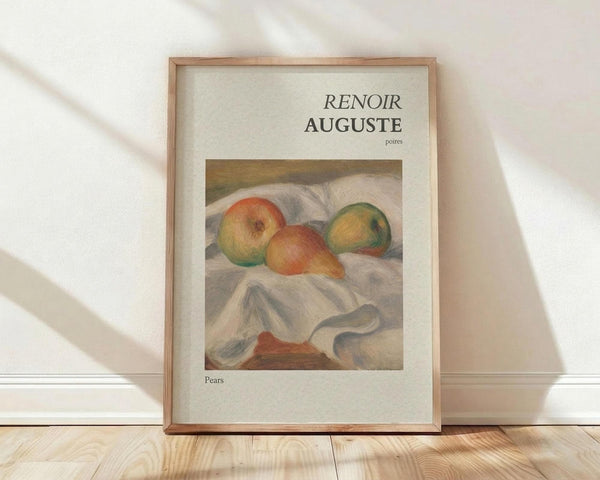 May include: Framed art print featuring Auguste Renoir's soft impressionist still life of pears in warm yellows, oranges and greens resting on white draped fabric. The cream-colored poster shows "RENOIR AUGUSTE" and "Pears" text above and below the artwork. Natural wood frame leans against white wall on light wooden floor with gentle window shadows.