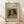 May include: Framed art print leaning against white wall on light wood floor. Print shows a small dog portrait with long dark ears and white face wearing a collar, painted in soft brown and cream tones. Text above reads "Pierre Auguste Renoir painting" and below "head of a dog 1870". Natural wood frame with light colored matting. Soft window light creates shadows on textured white wall.