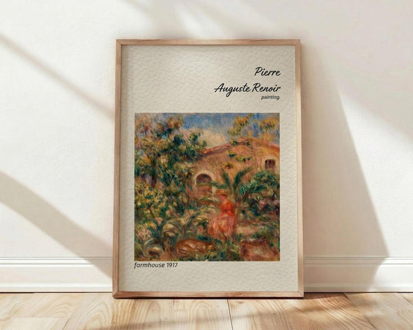May include: Framed art print featuring Pierre Auguste Renoir's impressionist painting of a Mediterranean farmhouse surrounded by lush green foliage and warm earth tones. The wooden frame sits against a white wall on light wood flooring with soft natural lighting creating diagonal shadows. The artwork shows Renoir's characteristic loose brushwork with vibrant greens, oranges, and blues depicting a rustic building nestled among trees and vegetation.