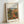 May include: Framed art print of Pierre-Auguste Renoir's impressionist painting featuring a Mediterranean farmhouse with terracotta roof surrounded by lush green foliage and trees. The artwork displays warm earth tones, soft brushstrokes, and vibrant colors typical of Renoir's style. Light wooden frame sits against white wall, showing the cream matting and black text identifying the artist and 1917 farmhouse subject.