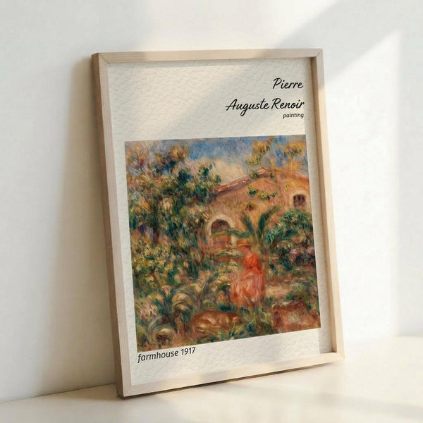 May include: Framed art print of Pierre-Auguste Renoir's impressionist painting featuring a Mediterranean farmhouse with terracotta roof surrounded by lush green foliage and trees. The artwork displays warm earth tones, soft brushstrokes, and vibrant colors typical of Renoir's style. Light wooden frame sits against white wall, showing the cream matting and black text identifying the artist and 1917 farmhouse subject.