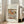 May include: Framed art print leaning against white wall next to beige upholstered chair in bright room with large windows. Print features soft-toned still life painting of three pears on draped white fabric, displayed in light wood frame with white matting and museum-style text layout.