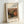 May include: A framed art print leaning against a white wall on a light surface. The print features a still life painting of pomegranates and figs in warm earth tones with rich reds, greens, and browns. Text reads "RENOIR AUGUSTE" at the top with "grenade et figues" below, and "Pomegranate and figs" at the bottom. The simple wooden frame has a natural light wood finish and white matting surrounds the artwork.