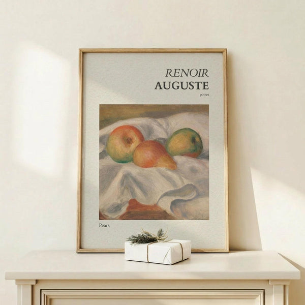 May include: Framed art print displaying Auguste Renoir's impressionist painting of three pears on white fabric draping. The pears show soft oranges, greens, and yellows with characteristic brushwork. Light wood frame with white matting, positioned on pale wooden surface alongside small wrapped gift with twine and evergreen sprig. Neutral beige wall background with natural lighting creating gentle shadows.