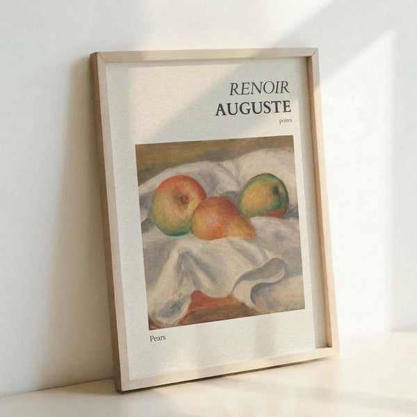 May include: Framed art print leaning against white wall showing Renoir's impressionist still life painting of colorful pears on white fabric. The artwork features soft brushstrokes in warm orange, yellow and green tones. Text reads "RENOIR AUGUSTE" at top and "Pears" at bottom on cream-colored background. Simple light wood frame casts gentle shadow on wall.