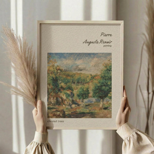 May include: Person in cream clothing holding framed art print featuring Renoir's impressionist landscape painting of lush green chestnut trees in countryside setting with soft brushstrokes in greens, browns, and blues. Light wood frame with beige matting displays against white curtained window with dried wheat stems visible beside frame.