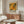 May include: Framed exhibition poster featuring abstract expressionist artwork in warm orange, yellow and green tones with "POLLOCK" text, displayed above wooden sideboard in modern living room with white curved chair, glass coffee table, and floor lamp
