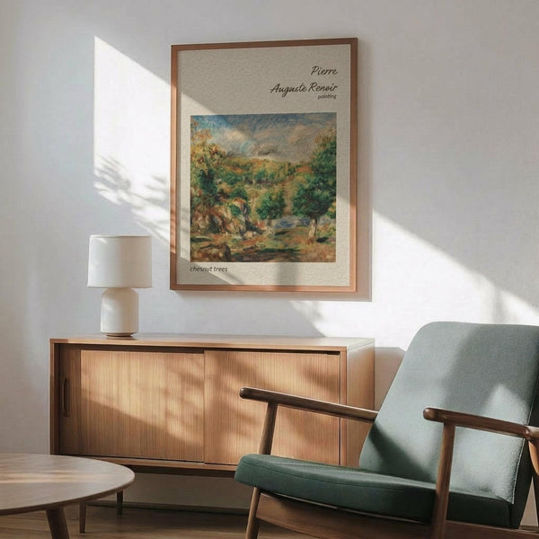 May include: Framed Renoir landscape print hanging on white wall above wooden credenza with white table lamp. Green upholstered mid-century modern armchair with wooden frame sits nearby. Poster shows impressionist painting of countryside scene with chestnut trees, rolling hills, and soft brushstrokes in greens, browns, and blues. Natural sunlight creates shadows across the minimalist room setting.