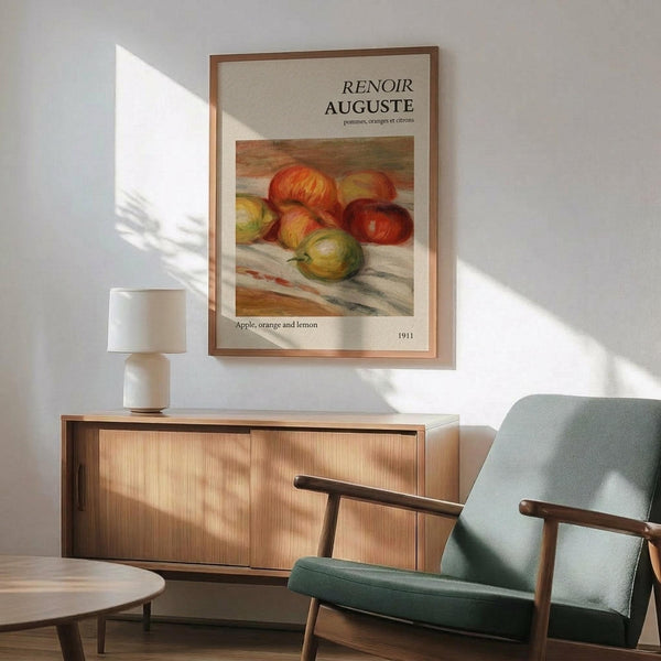 May include: Framed art print of Renoir's fruit still life painting showing red apples, orange, and lemon on white cloth, displayed above wooden sideboard with white ceramic table lamp in modern living room with mint green mid-century armchair and natural sunlight streaming across white walls