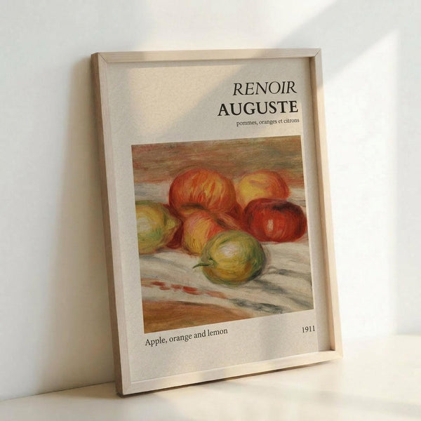 May include: Framed art print featuring Renoir's 1911 still life painting of apples, oranges and a lemon in warm red, yellow and green tones. The poster has white matting with French and English titles, displayed in a light wood frame leaning against a white wall with soft natural lighting.