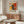 May include: Abstract art poster with vibrant red, yellow, and black paint splatters and gestural brushstrokes, displayed in thin brown frame above walnut credenza in modern living room with white upholstered chair, glass coffee table, and brass floor lamp