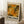 May include: Framed exhibition poster featuring abstract artwork in warm autumn colors - oranges, yellows, and greens with flowing organic patterns. The poster displays "POLLOCK" in bold black letters with exhibition details below. Shown leaning against white wall on textured rug next to wooden side table with coffee cup and cozy throw blanket.