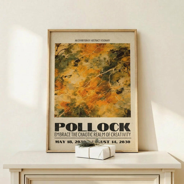 May include: Framed exhibition poster with abstract artwork in warm oranges, yellows and greens displayed on light wood console table. Poster features bold black text and dates, housed in natural wood frame. Small white wrapped gift with greenery sits beside frame against cream colored wall.