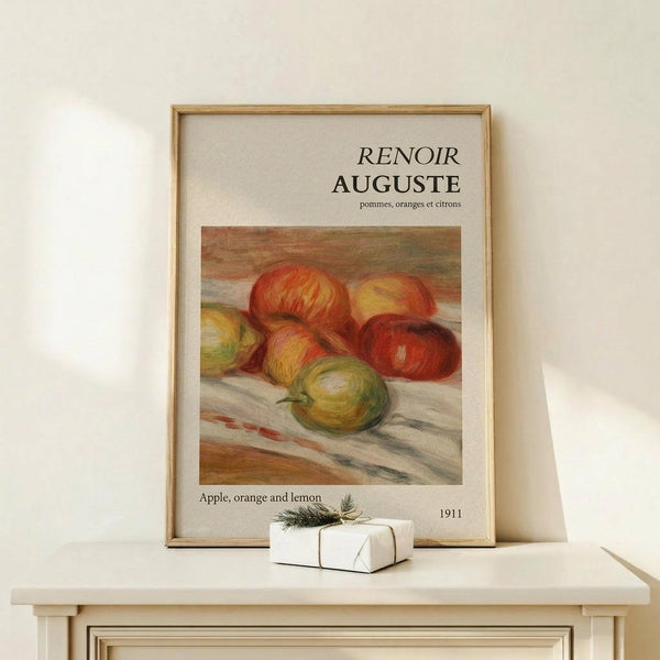 May include: Framed art print featuring Renoir's 1911 still life painting of colorful apples, oranges and a lemon arranged on white fabric. The poster has cream matting with black text in French and English. Displayed on a light wood console table beside a small white wrapped gift with twine and evergreen sprig against a neutral beige wall.