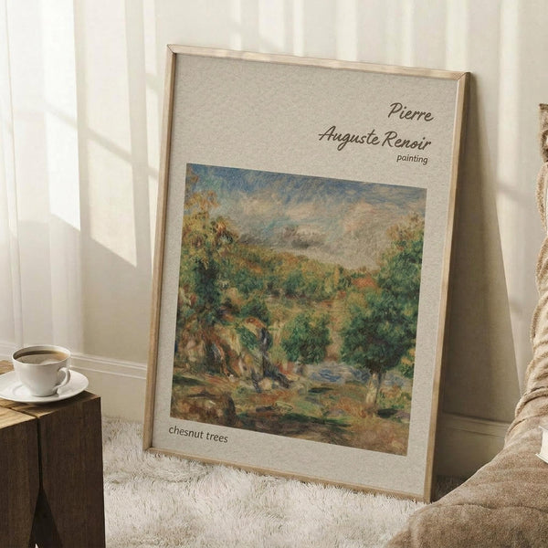 May include: Framed Renoir landscape painting print showing lush green chestnut trees in an impressionist style, displayed in a light wood frame against white wall corner. The artwork features soft brushstrokes in greens, blues and earth tones depicting a pastoral scene. Scene includes white coffee cup on wooden block and beige textured throw blanket nearby, creating a cozy home interior setting with natural lighting.