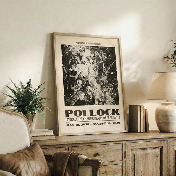 May include: Black and white abstract art poster with paint splatter design in wooden frame, displayed on rustic wooden console table alongside fern plant, books, and ceramic vase in neutral-toned living room setting