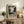 May include: Black and white abstract art poster with paint splatter design in light wood frame, displayed on rustic wooden sideboard with leather chair, potted fern, ceramic vase, and stacked books in warm-toned living room setting