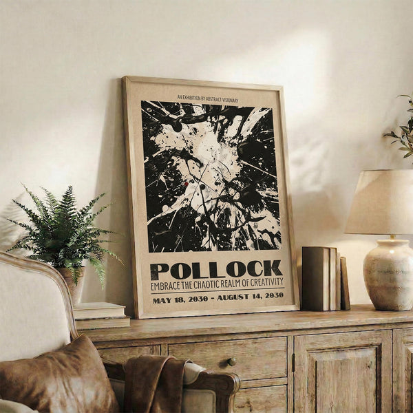 May include: Black and white abstract art poster with paint splatter design in light wood frame, displayed on rustic wooden sideboard with leather chair, potted fern, ceramic vase, and stacked books in warm-toned living room setting