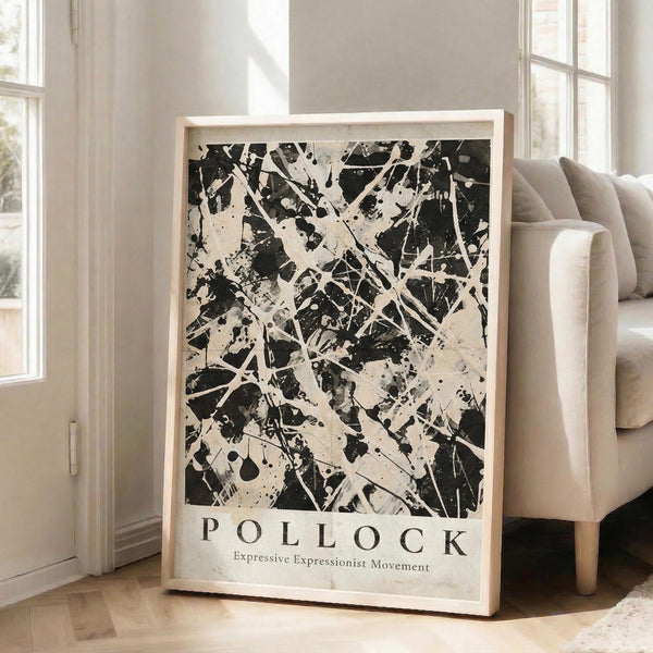 May include: Large framed abstract art poster with black paint splatters and white drips on cream background, leaning against white wall next to beige sofa. Bold text reads "POLLOCK" with subtitle below. Natural lighting streams through tall windows, creating shadows on light wood floors in minimalist living room setting.