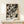 May include: Black and white abstract expressionist art print displayed in light wood frame on cream wooden surface against beige wall. Artwork features dynamic paint splatters, drips, and gestural marks in monochromatic palette. Small wrapped gift box with evergreen sprig sits beside frame. Print shows bold contrast between dark paint strokes and light background with energetic, spontaneous brushwork typical of action painting style.