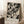 May include: Black and white abstract expressionist art print with chaotic paint splatters, drips, and gestural brushstrokes in wooden frame, leaning against white wall next to wooden stool with coffee cup and saucer, on textured cream rug beside beige blanket in bright room with window light.