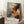 May include: Abstract expressionist art print with dynamic paint splatters and brushstrokes in orange, red, black, and blue against light blue background, displayed in light wood frame leaning against white wall next to white coffee cup on wooden stool and beige textured rug