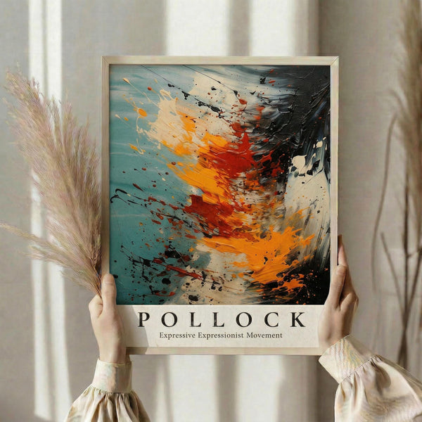 May include: Person holding framed abstract expressionist art print featuring dynamic paint splatters and brushstrokes in turquoise, orange, red, and black colors. Light wooden frame against neutral curtained background with dried pampas grass visible to the side. Bold gestural movements create energetic composition with paint drips and textural elements throughout the square format artwork.