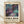 May include: Framed abstract art poster with swirling cosmic design in deep purples, teals, and gold accents, featuring flowing lines and circular elements resembling a galaxy or nebula. Light wooden frame against white textured wall on wooden floor with soft natural lighting creating diagonal shadows.