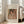 May include: A framed art print leaning against a white wall beside a beige upholstered chair. The poster features a Renoir painting of a woman with dark hair wearing a pearl necklace and flowing fabric in warm peachy tones. The print has "Pierre Auguste Renoir painting" at the top and "Woman with black hair" at the bottom on a cream background with light wood frame.