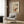 May include: Framed vintage Japanese woodblock print showing figure in red clothing walking through snowy mountain landscape with walking stick. Displayed on wood paneled wall above beige upholstered armchair with geometric patterned pillow. Modern reading corner with brass floor lamp and dark side table holding open book.