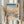 May include: Hands holding a framed reproduction of a Japanese woodblock print showing a snowy winter landscape with Mount Fuji, bare trees, a blue stream, small figures crossing a bridge, and traditional buildings. The artwork features soft blues, whites, and peach tones typical of ukiyo-e style. Light wood frame against cream curtains with dried pampas grass visible on the left side.
