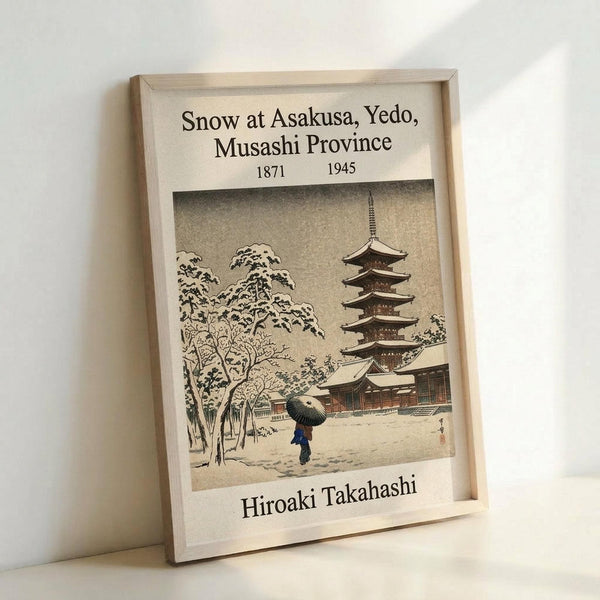 May include: Framed vintage Japanese woodblock print showing a snowy winter scene with a multi-story pagoda temple, bare snow-covered trees, and a figure with a dark umbrella walking through white snow. The artwork features muted earth tones and traditional ukiyo-e style illustration. The print is displayed in a light wooden frame leaning against a white wall, with text identifying the location as Asakusa and artist as Hiroaki Takahashi with dates 1871-1945.