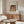 May include: Renoir reproduction poster displayed in modern minimalist room with wooden sideboard, white curved chair, glass coffee table, and warm natural lighting. The vintage art print shows a woman with dark hair wearing flowing fabrics in soft peachy tones, matted and framed in thin brown frame against cream wall.