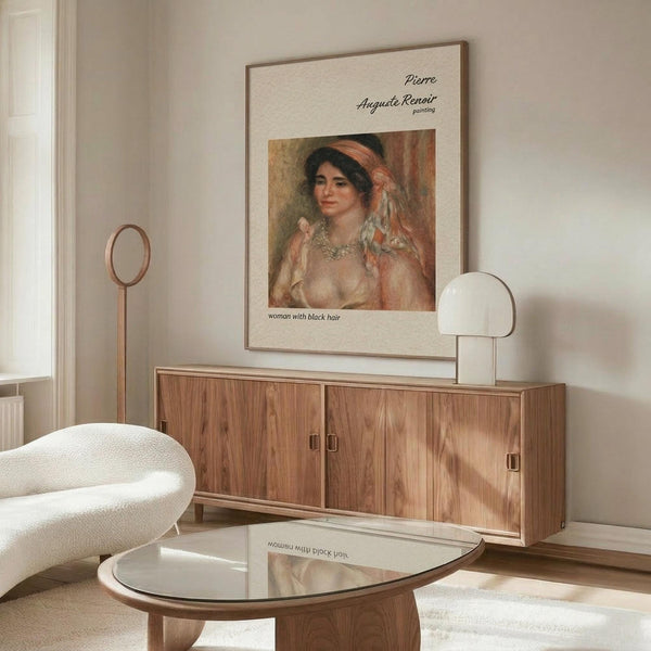 May include: Renoir reproduction poster displayed in modern minimalist room with wooden sideboard, white curved chair, glass coffee table, and warm natural lighting. The vintage art print shows a woman with dark hair wearing flowing fabrics in soft peachy tones, matted and framed in thin brown frame against cream wall.