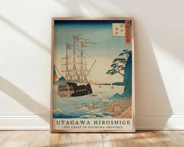 May include: Framed Japanese woodblock print reproduction showing a large sailing ship with multiple masts and colorful flags on choppy blue-green waters near a rocky coastline with pine trees. The vintage-style artwork features traditional ukiyo-e colors and composition with Japanese text in the upper right corner. The wooden frame leans against a white wall on light wood flooring with natural window light creating soft shadows.