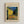 May include: Framed poster print of Van Gogh's famous café terrace night scene hanging on white textured wall. The artwork shows a yellow-lit café with outdoor seating under a starry blue evening sky, cobblestone street, and buildings in warm yellows and cool blues. Light wood frame surrounds cream-colored matting with black text identifying the artist, painting title, and 1888 date.