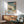 May include: Framed Japanese woodblock print showing sailing ships on blue-green water with coastal landscape, displayed above wooden sideboard with white ceramic lamp in modern living room setting with mint green upholstered chair featuring wooden arms