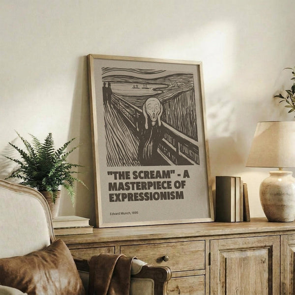 May include: Black and white reproduction of Munch's famous expressionist artwork showing a figure with hands to face in anguish on a bridge, displayed in light wood frame on rustic wooden sideboard. Room features neutral walls, fern plant, ceramic vase, stacked books, and beige upholstered chair with leather cushion. Poster includes bold text identifying the artwork as a masterpiece of expressionism.
