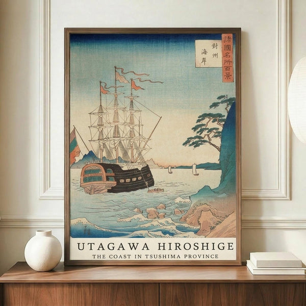 May include: Japanese woodblock print poster featuring a Western sailing ship with multiple masts and colorful flags on choppy blue-green waves, with rocky coastline and pine tree visible on right side. Japanese text cartouche in upper right corner. Print displayed in brown frame on wooden credenza next to white ceramic vase and stacked books in neutral-toned room with white walls and molding.