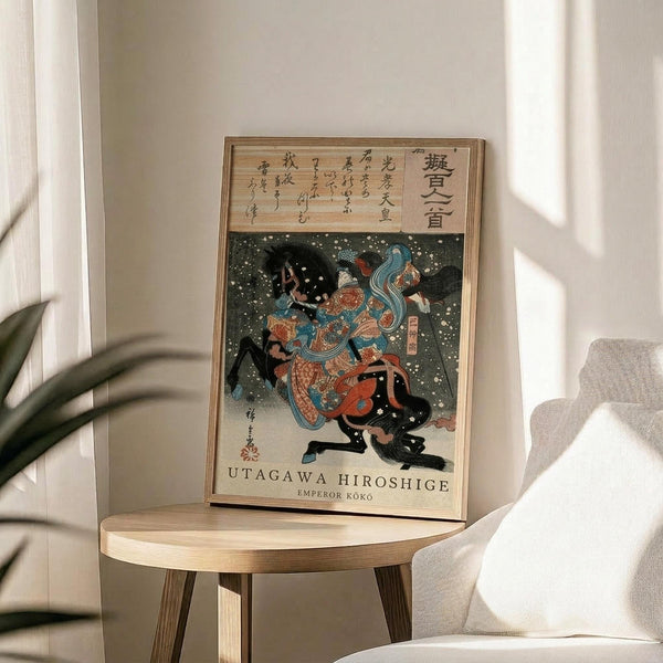 May include: Framed Japanese woodblock print artwork displayed on a light wood round side table next to a beige upholstered chair. The print features two figures in traditional dress with flowing blue hair against a dark starry background, with Japanese text above. Natural sunlight streams across the neutral-toned room setting with a plant visible in the corner.