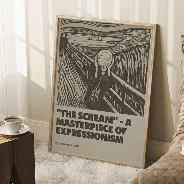 May include: Framed poster print featuring Edvard Munch's The Scream artwork in black and white, showing the iconic figure with hands to face on a bridge with two silhouettes in background. Bold text below reads "THE SCREAM - A MASTERPIECE OF EXPRESSIONISM" with artist name and date. Light wooden frame leaning against white wall corner next to cozy armchair and wooden side table with coffee cup on white textured rug.