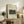May include: Framed art print of Henri Rousseau's jungle painting featuring a lion attacking an antelope amid lush green foliage, displayed on rustic wooden sideboard with fern plant, books, ceramic vases, and beige upholstered chair in neutral-toned living room setting