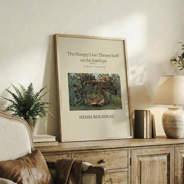 May include: Framed art print of Henri Rousseau's jungle painting featuring a lion attacking an antelope amid lush green foliage, displayed on rustic wooden sideboard with fern plant, books, ceramic vases, and beige upholstered chair in neutral-toned living room setting